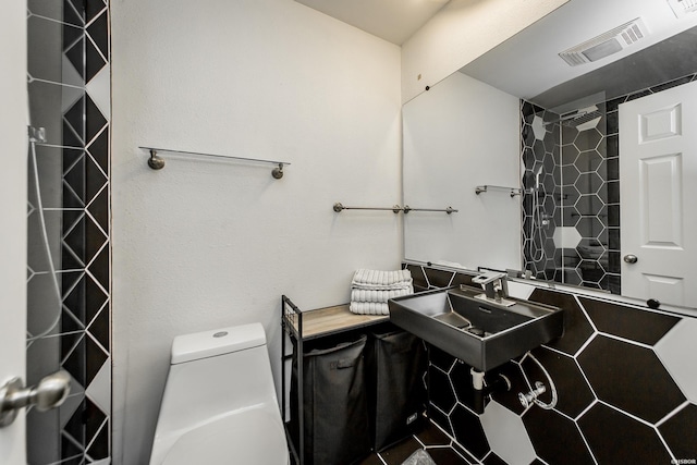 full bath with toilet, tiled shower, visible vents, and a sink