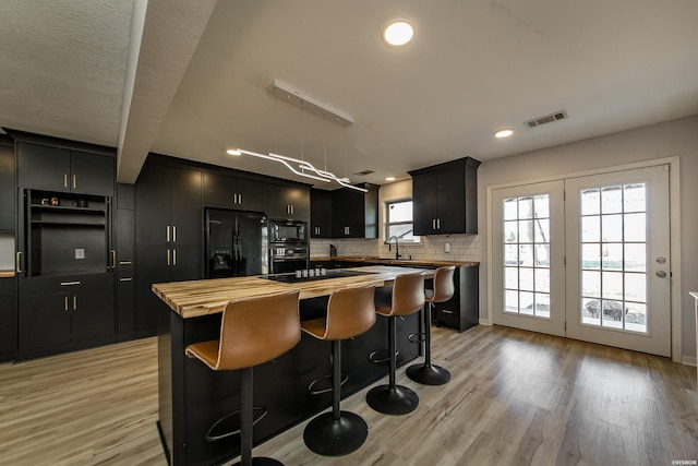 kitchen with visible vents, black appliances, dark cabinetry, a center island, and wooden counters