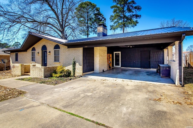 ranch-style house featuring metal roof, brick siding, concrete driveway, and a chimney