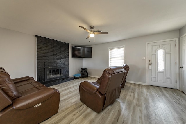 living room featuring a ceiling fan, a brick fireplace, light wood-style flooring, and baseboards