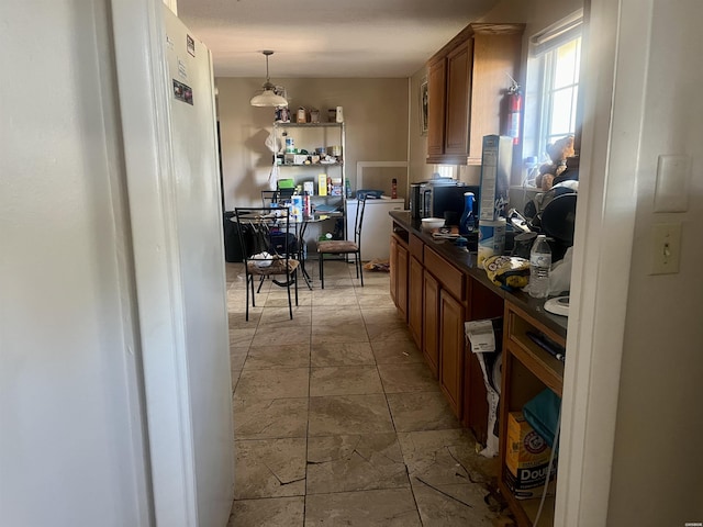 kitchen featuring dark countertops, pendant lighting, brown cabinets, and freestanding refrigerator