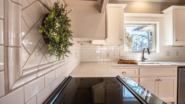 kitchen featuring light stone counters, backsplash, a sink, white cabinetry, and stainless steel dishwasher