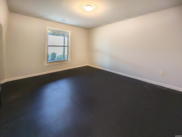 empty room featuring concrete floors, visible vents, and baseboards