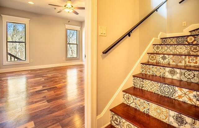 stairway featuring ceiling fan, plenty of natural light, wood finished floors, and baseboards