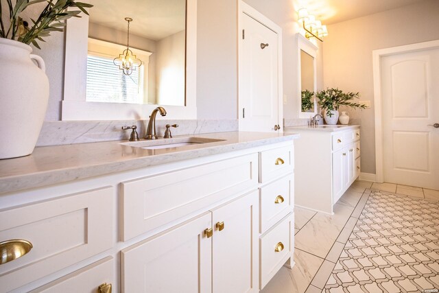 bathroom with marble finish floor, a chandelier, two vanities, and a sink