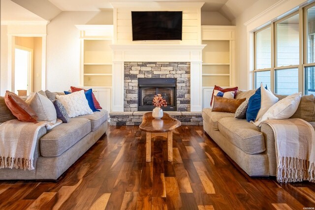 living area with lofted ceiling, a stone fireplace, dark wood finished floors, and built in shelves