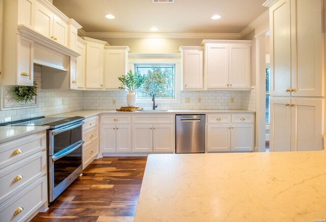 kitchen featuring a sink, white cabinets, appliances with stainless steel finishes, dark wood-style floors, and crown molding