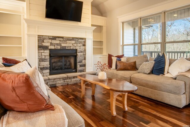 living area featuring dark wood-type flooring, vaulted ceiling, a stone fireplace, and built in shelves