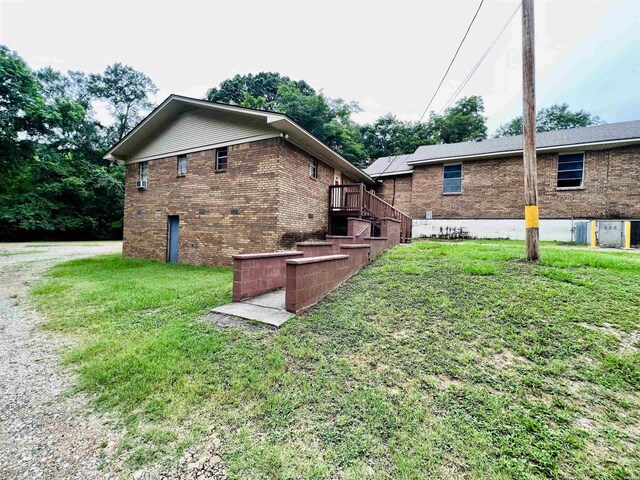 view of side of home with driveway, brick siding, stairway, and a lawn