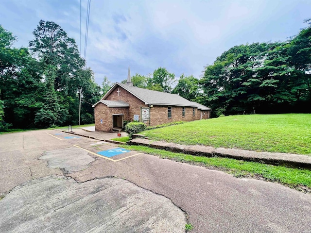 view of side of home with uncovered parking, brick siding, and a lawn