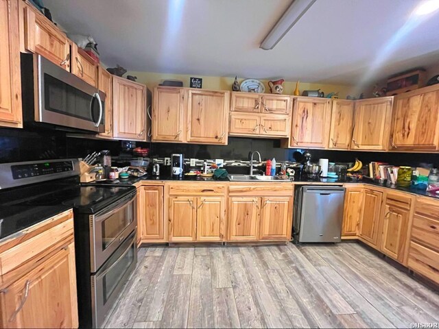 kitchen with appliances with stainless steel finishes, light wood-style floors, a sink, and light brown cabinetry