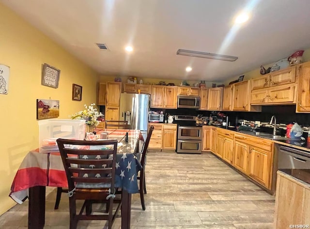 kitchen with light wood-style flooring, a sink, visible vents, appliances with stainless steel finishes, and dark countertops