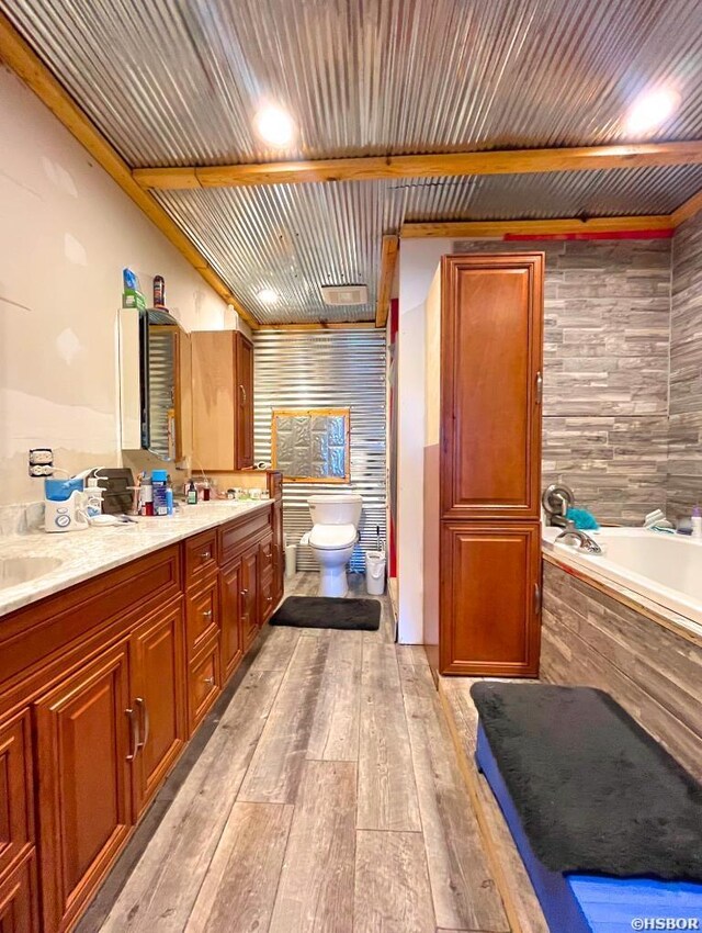 bathroom with toilet, double vanity, wood finished floors, and a washtub