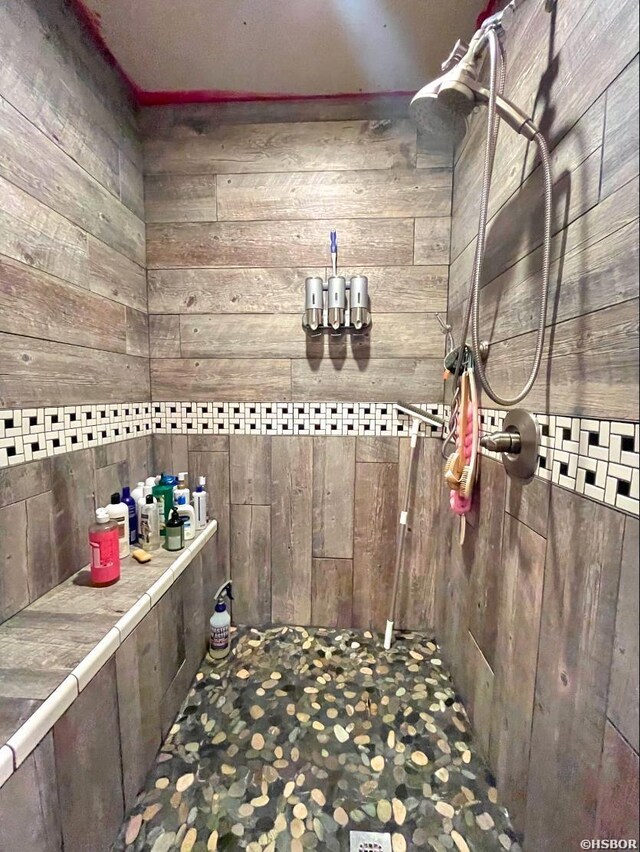 bathroom featuring tiled shower and wooden walls