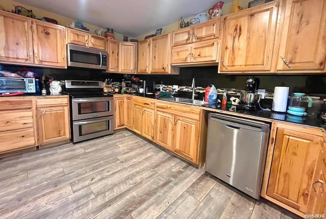 kitchen featuring a toaster, stainless steel appliances, a sink, light wood finished floors, and dark countertops