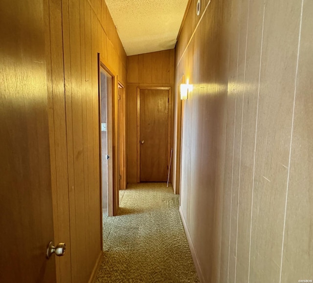 hallway featuring carpet floors, wooden walls, and a textured ceiling