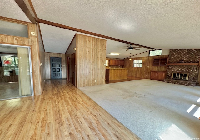 unfurnished living room featuring a fireplace, lofted ceiling with beams, wood walls, a textured ceiling, and light wood-type flooring