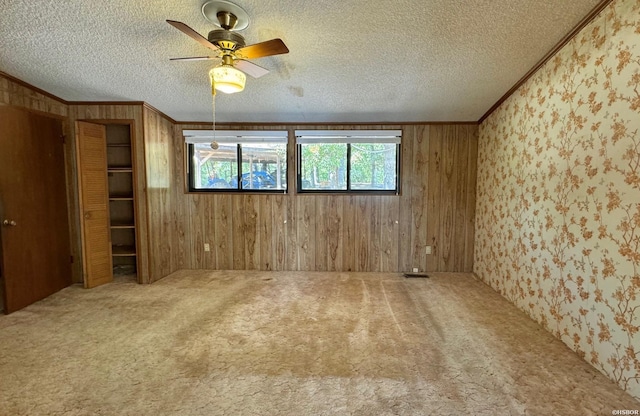 unfurnished room with a textured ceiling, wooden walls, a ceiling fan, ornamental molding, and carpet