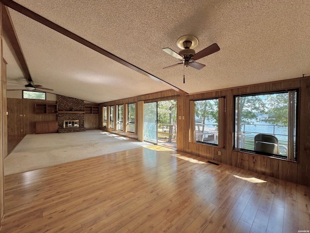 unfurnished living room with a brick fireplace, light wood-style floors, vaulted ceiling with beams, a textured ceiling, and wood walls