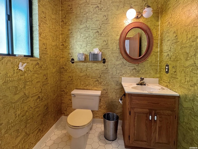 half bathroom featuring toilet, vanity, baseboards, tile patterned floors, and wallpapered walls