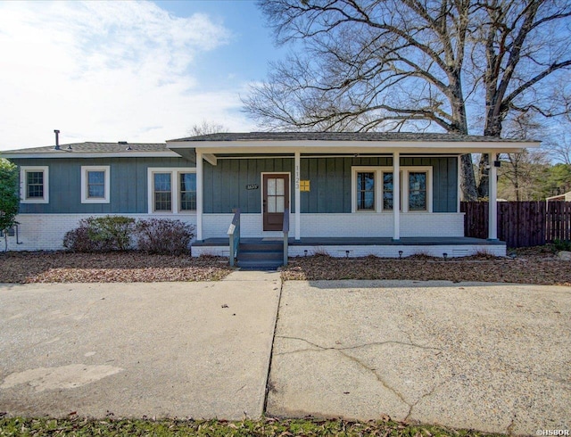 view of front of property with a porch, board and batten siding, fence, and brick siding