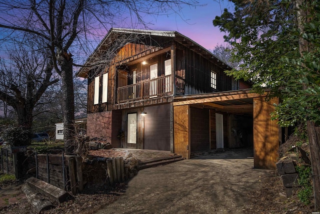 back of property at dusk featuring driveway and a balcony