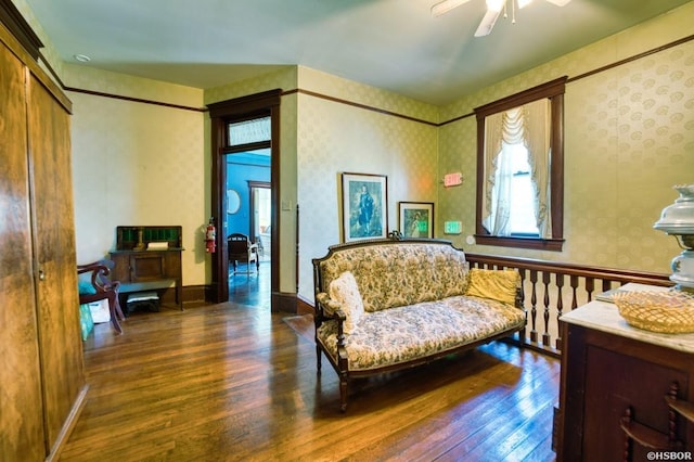 living area with a ceiling fan, dark wood-style flooring, baseboards, and wallpapered walls