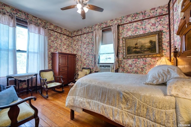 bedroom with cooling unit, wood finished floors, multiple windows, and wallpapered walls