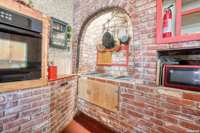 kitchen featuring brick wall, wainscoting, wood finished floors, and oven