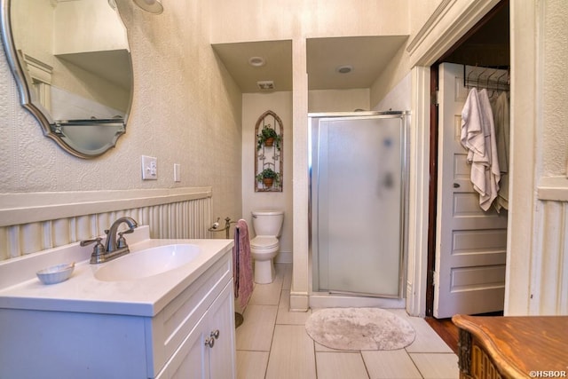 bathroom with a stall shower, a textured wall, toilet, vanity, and a closet