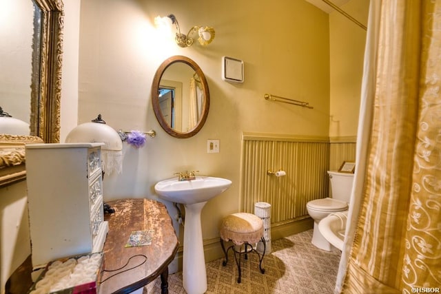 bathroom with toilet, a sink, and wainscoting