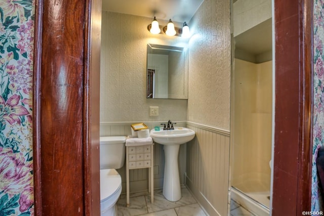 bathroom with a textured wall, toilet, a wainscoted wall, a sink, and a shower stall