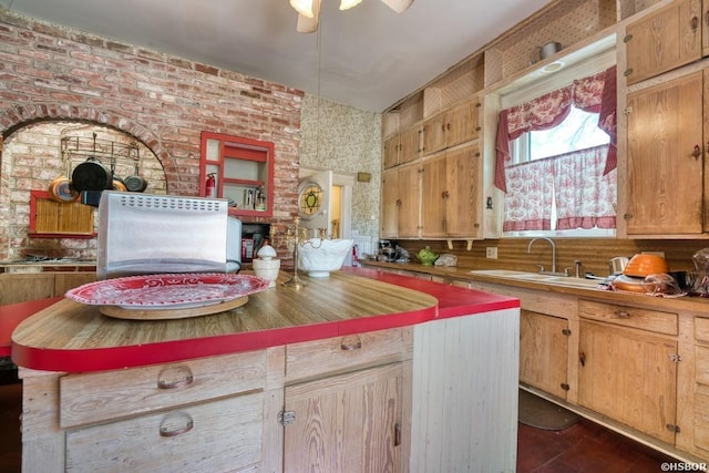 kitchen featuring brown cabinetry, a kitchen island, a sink, brick wall, and ceiling fan