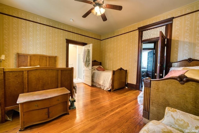 bedroom featuring wallpapered walls, a ceiling fan, baseboards, and wood finished floors