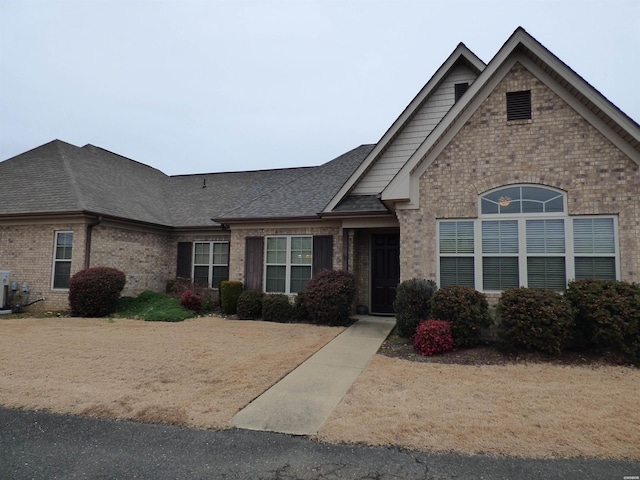 view of front of house featuring brick siding, a shingled roof, and a front yard