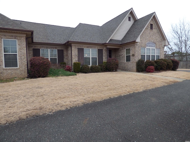 view of front of home with a shingled roof, a front yard, and brick siding