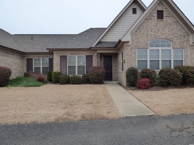 view of front of home with a shingled roof and brick siding