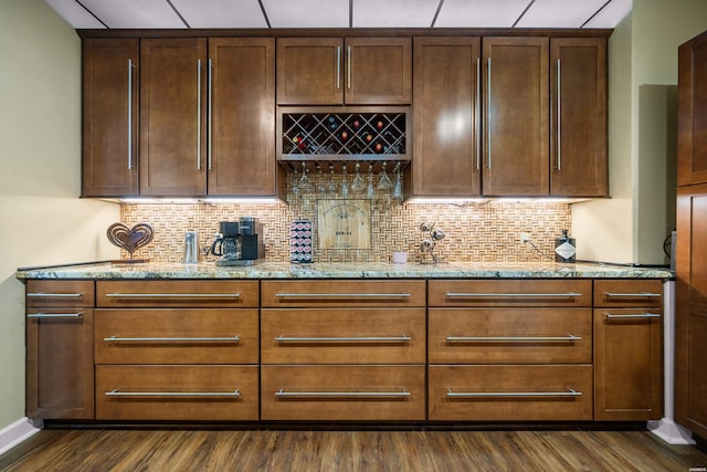 kitchen featuring backsplash, light stone countertops, dark wood-type flooring, and baseboards
