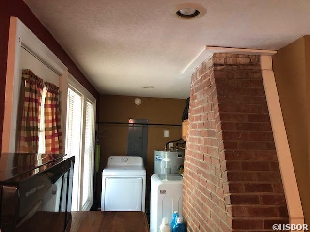 washroom featuring washing machine and clothes dryer, brick wall, water heater, and laundry area