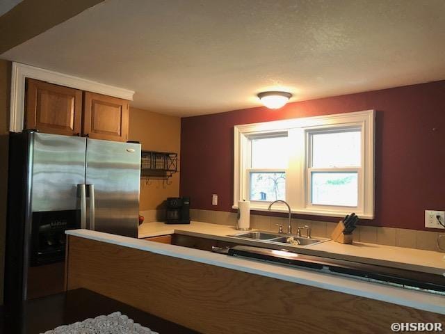 kitchen featuring light countertops, stainless steel refrigerator with ice dispenser, brown cabinets, and a sink