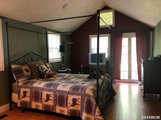 bedroom with wood finished floors, visible vents, lofted ceiling, and baseboards