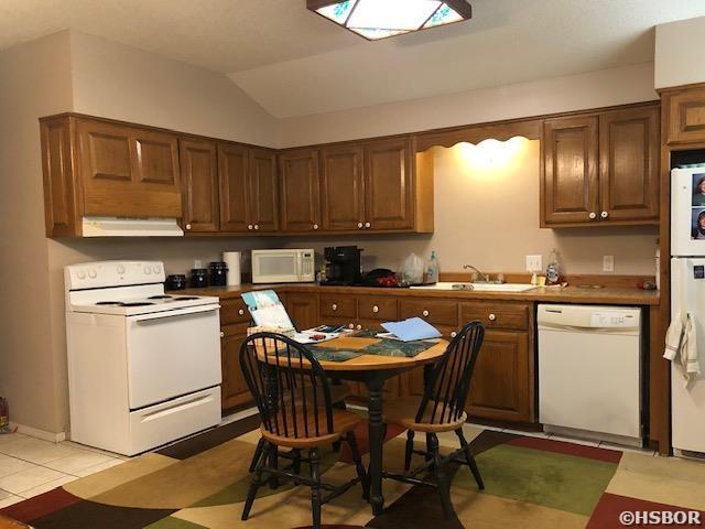 kitchen featuring a sink, brown cabinets, white appliances, lofted ceiling, and under cabinet range hood