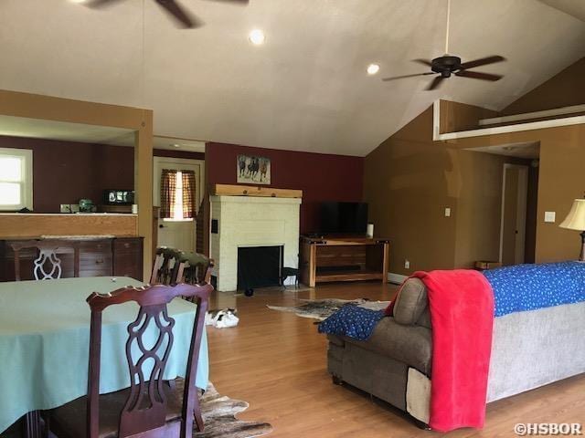 living area with vaulted ceiling, wood finished floors, a fireplace, and ceiling fan