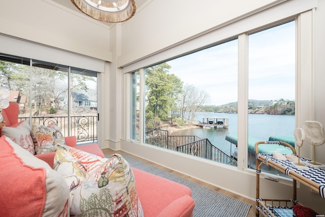 sunroom / solarium featuring wood finished floors, a water view, and baseboards