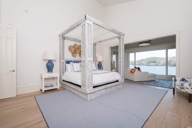 bedroom featuring light wood-type flooring, a water view, and baseboards