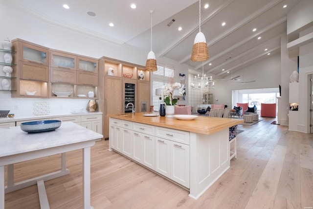 kitchen featuring decorative backsplash, open shelves, high vaulted ceiling, open floor plan, and a center island with sink