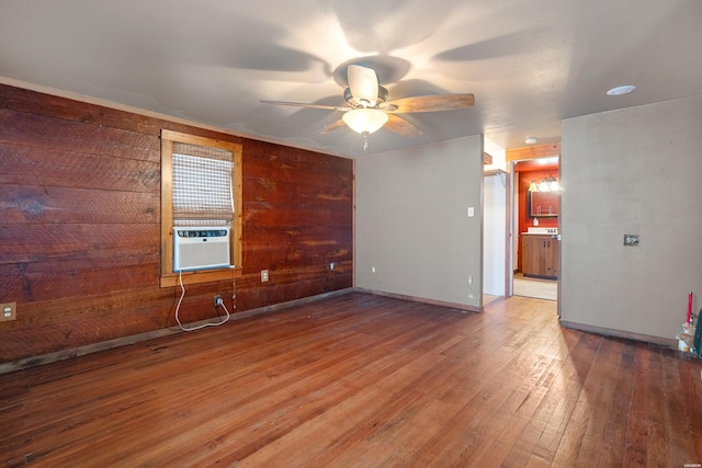 empty room featuring a ceiling fan, wood walls, wood finished floors, cooling unit, and baseboards