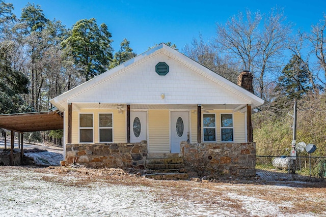 view of front of home featuring an attached carport, stone siding, and a chimney