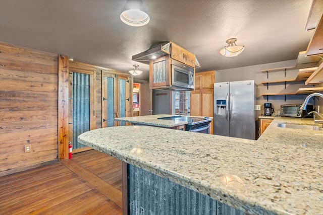 kitchen featuring a peninsula, dark wood-type flooring, wood walls, a sink, and appliances with stainless steel finishes