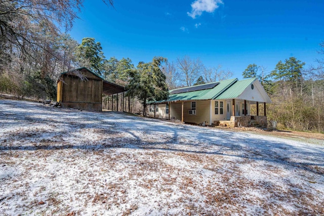 snow covered property with gravel driveway, a porch, metal roof, and a detached carport